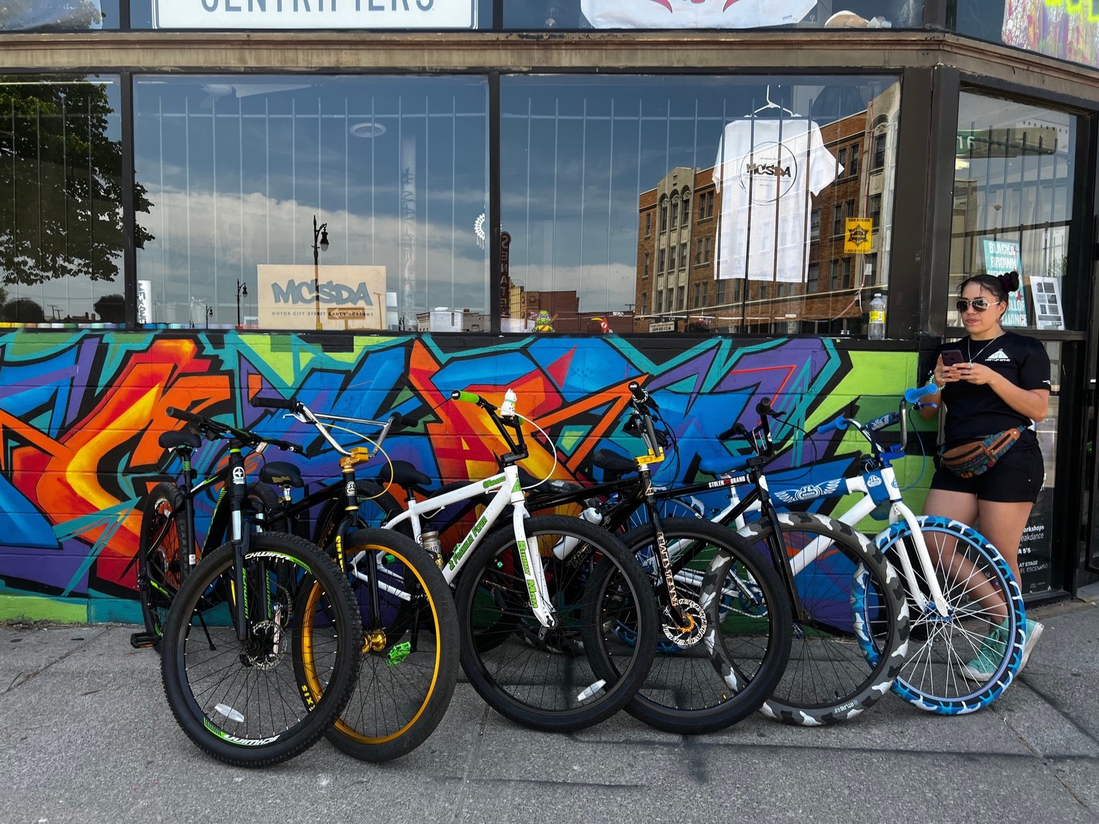 A lineup of custom BMX bikes against the shop's graffiti mural, with the Street Wheels Culture Spot logo overlaid
