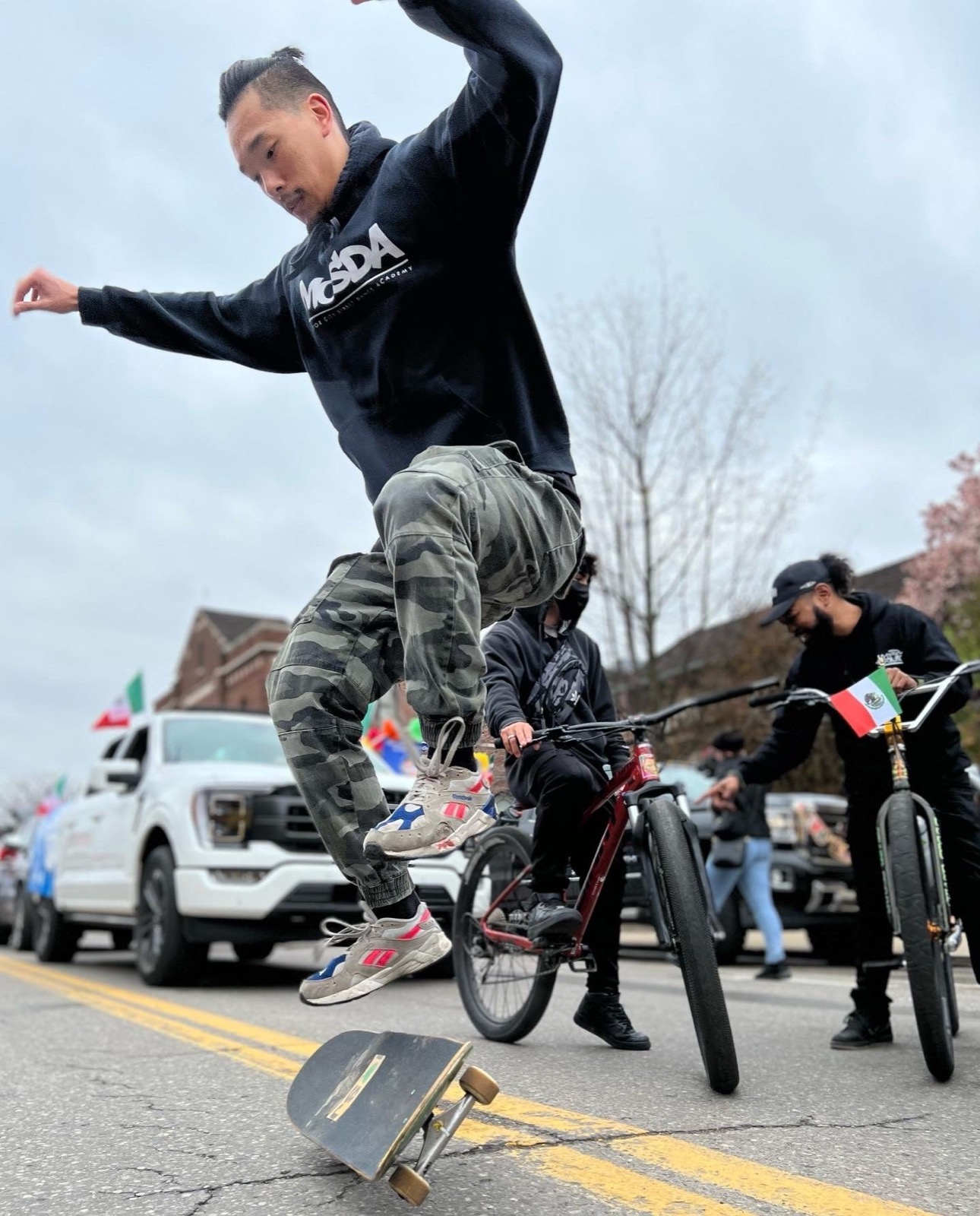 A rider performing a skateboard trick off a BMX bike in the street